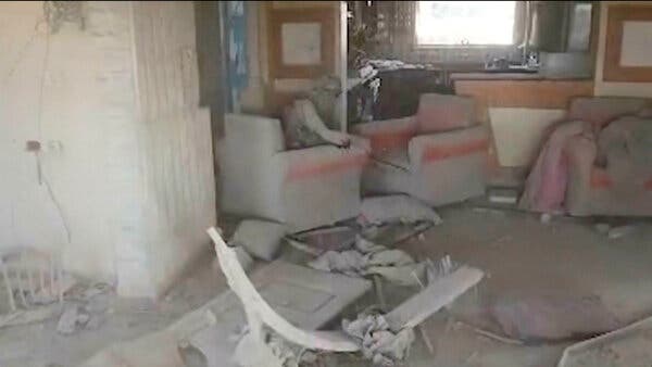 A video still shows a man sitting in a chair in a heavily damaged and dusty room.