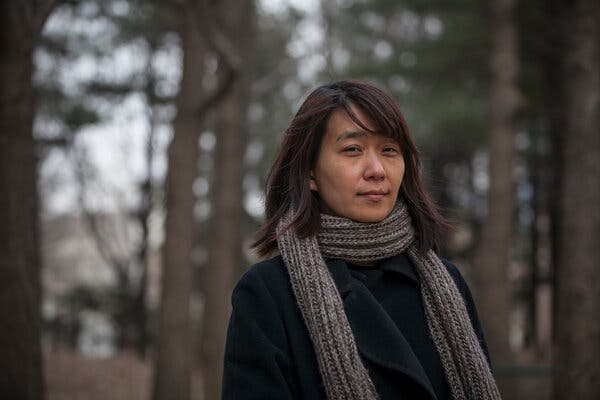 Han Kang, wearing a dark coat and gray scarf, outside with trees behind her.