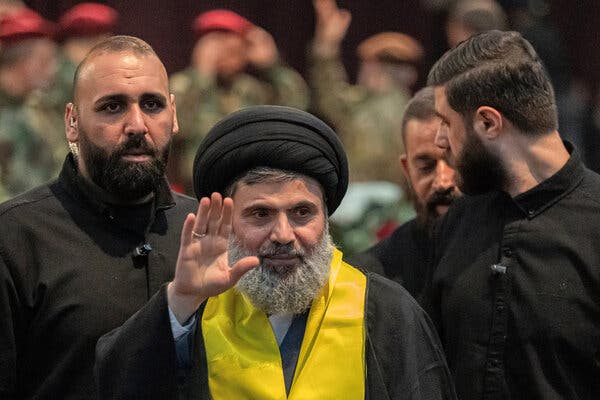 A man surrounded by a security detail waves.