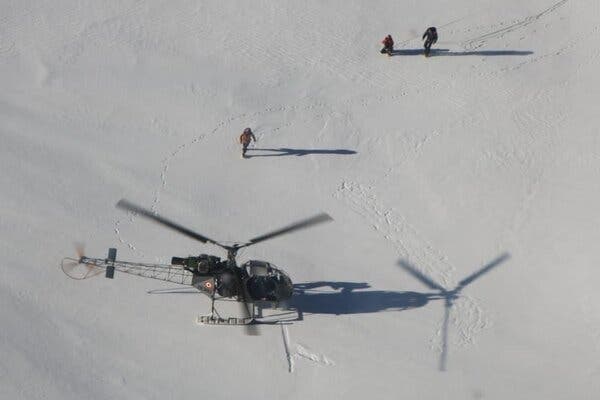 A helicopter lands on snow as people walk toward it.