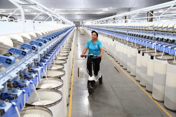 A woman wearing a turquoise T-shirt rides a white scooter down an aisle of white barrels. 