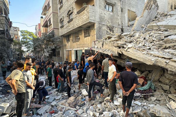 People stand on rubble in front of a heavily damaged building.