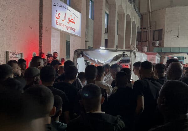 A crowd of people around a vehicle at the emergency entrance of a hospital. 