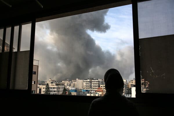 A large cloud of gray smoke appears over an urban scene out a window. 