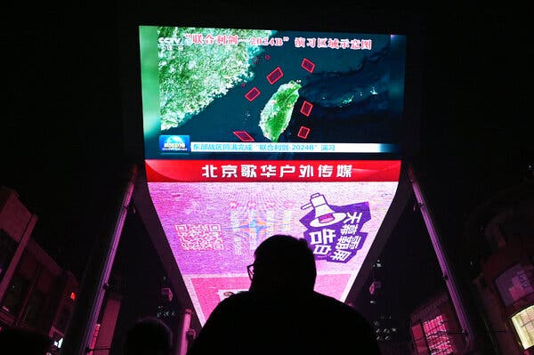 A man watches a news program about Chinese military drills surrounding Taiwan, on a giant screen outside a shopping mall in Beijing.