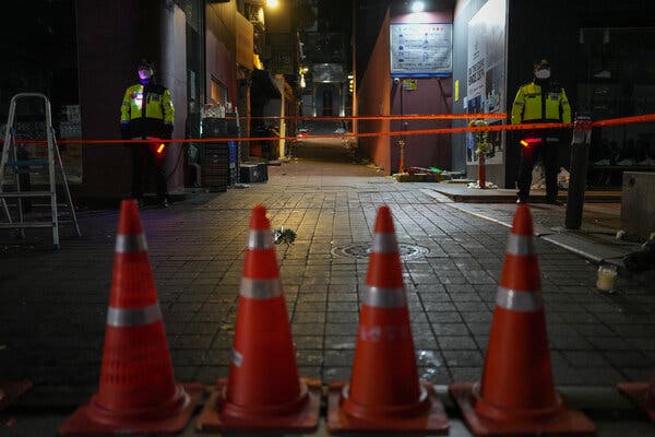 An alleyway blocked off by four traffic cones, two sets of police tape and two police officers.