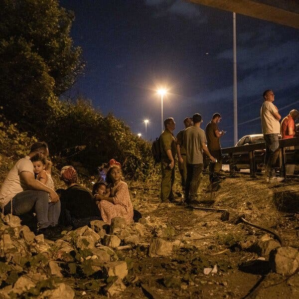 People sit on the side of a road behind a guard rail.