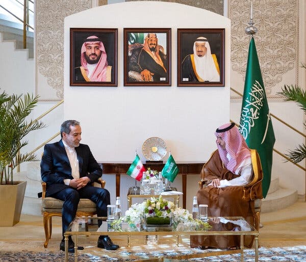 Iran’s foreign minister, Abbas Araghchi, left, with the Saudi foreign minister, Prince Faisal bin Farhan al-Saud, sitting with framed portraits behind them. A small table bearing the Saudi and Iranian flags is between them. 