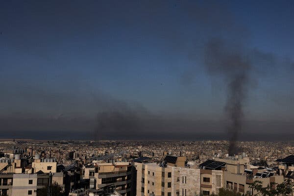 A cloud of black smoke rises over tall buildings.