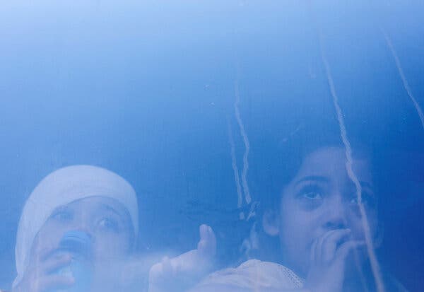 Two children, one with a bandaged head, looking out of a vehicle’s window. 