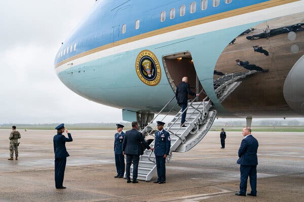 President Biden walks up the steps of Air Force One at Joint Base Andrews in Maryland. Several security officials stand at the base of the steps. 