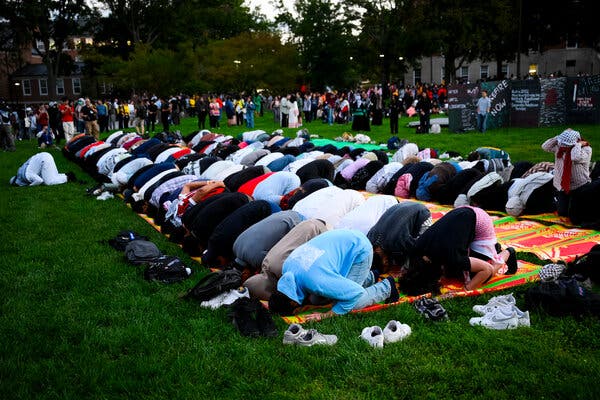 Rows of students kneel on prayer mats in the grass on the University of Maryland campus.