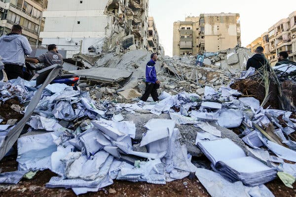 Five men standing amid rubble of buildings and lots of papers. 