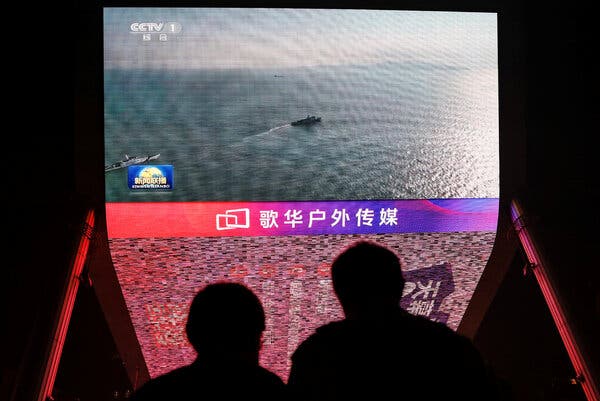 People look at a giant screen showing news footage of military drills conducted in the Taiwan Strait.