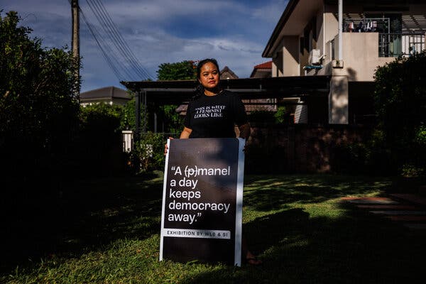 A woman posing with a poster that reads: “A manel a day keeps democracy away.” The m in manel is next to a crossed-out p, which would have made the word panel.