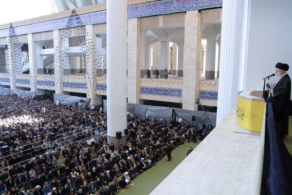 Ayatollah Ali Khamenei reads from a podium to a large crowd below him.