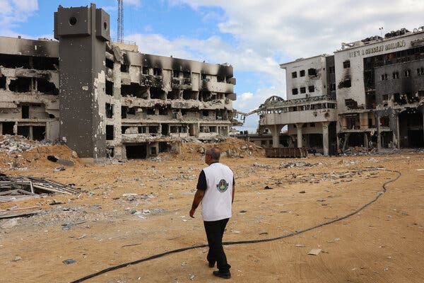 A man in a white shirt and dark pants walking by ruined buildings.