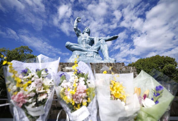 Bouquets of flowers are lined up near a statue that sits atop a memorial.