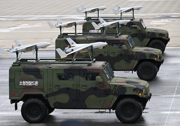 Three military vehicles carry small drones on top of them.