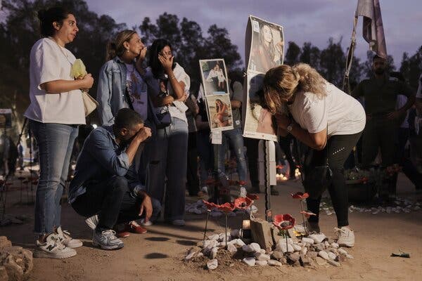 Distressed people stand around a makeshift memorial with large photos of victims.