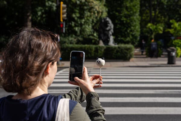 A person holding up a phone to take a photograph of a cake pop shaped like a panda.