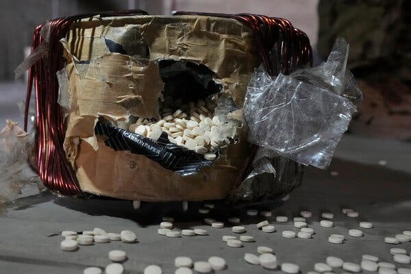 A package wrapped in wire and tape which is ripped open at the top, with white pills spilling out.