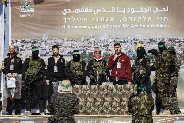 Masked men holding guns and wearing fatigues on a stage alongside three men who had been their hostages.