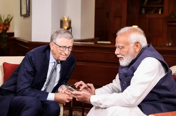 Bill Gates looks at his phone while Narendra Modi uses it.