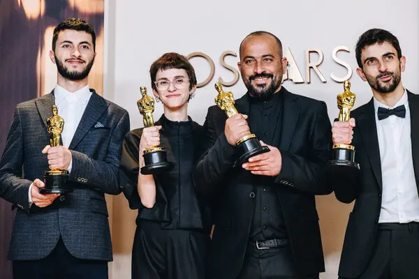 Four people hold Oscar statuettes.