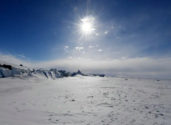 The icy plain stretches far into the distance under a blue sky and bright sun.