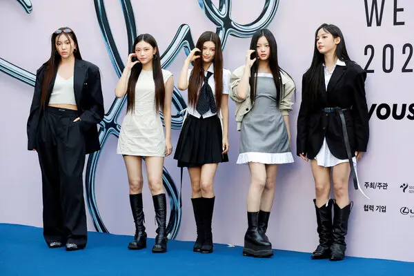 Five young women in stylish clothes pose for a photographer on a blue carpet.