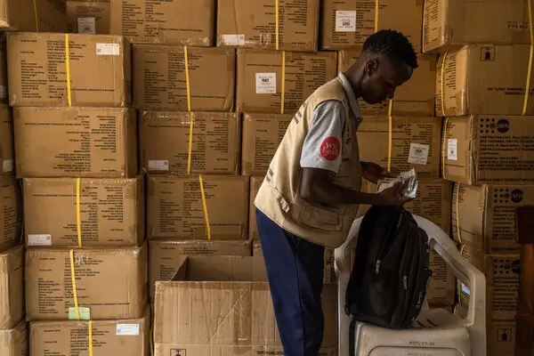 Andrea Minaj Casablanca in a work vest. Cardboard boxes are stacked in the background.