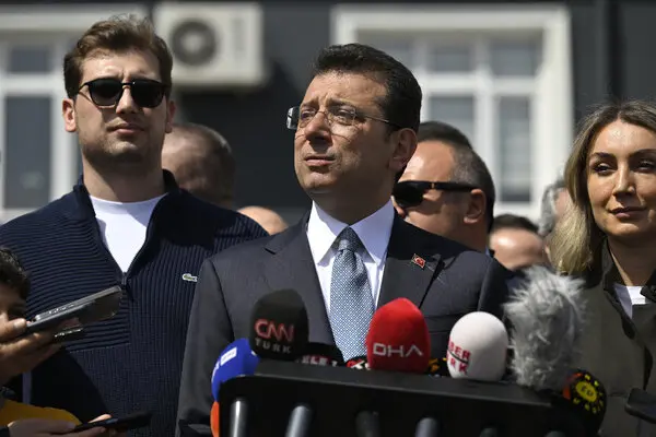 Istanbul Mayor Ekrem Imamoglu speaks at the podium with several people standing around him.