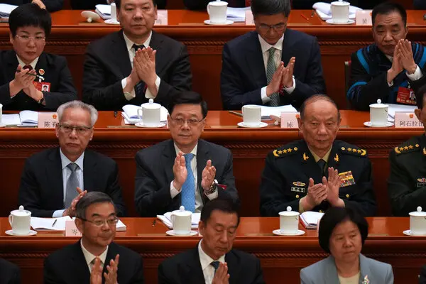 Men and women in suits or uniforms sit at narrow tables and applaud in the legislative chamber.