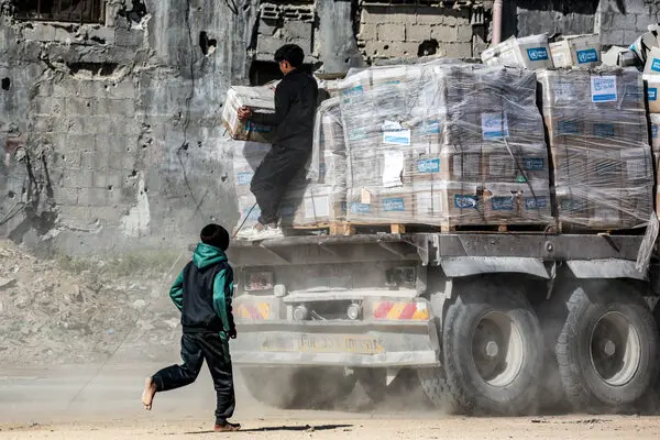 A boy (pictured behind) chases a heavy truck carrying many cardboard boxes containing food aid.