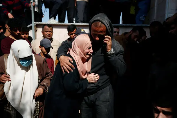 Two women in headscarves and a man in a hoodie are crying.