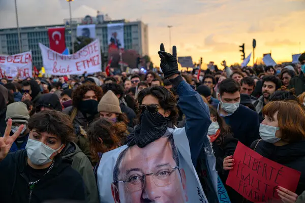 A dense crowd of young people, some holding placards and banners, at sunset.