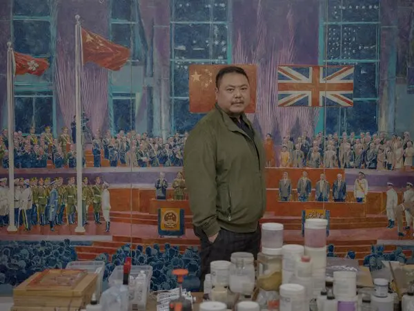 Chow Chun Fai stands in front of a large painting of the ceremony. Paint cans and other art supplies are on a table nearby.