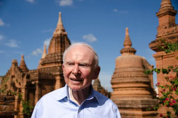 Roy L. Prosterman, a gray-haired man in a blue button-down shirt, stands in front of the historic building.