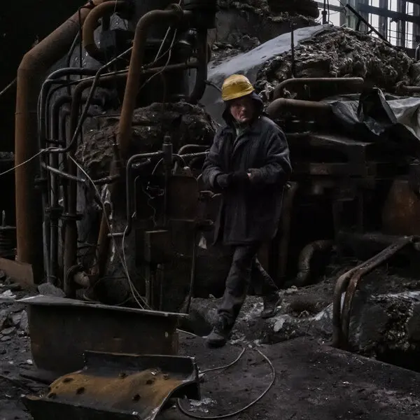 A man wearing a construction helmet walks through the twisted ruins of a metal building.