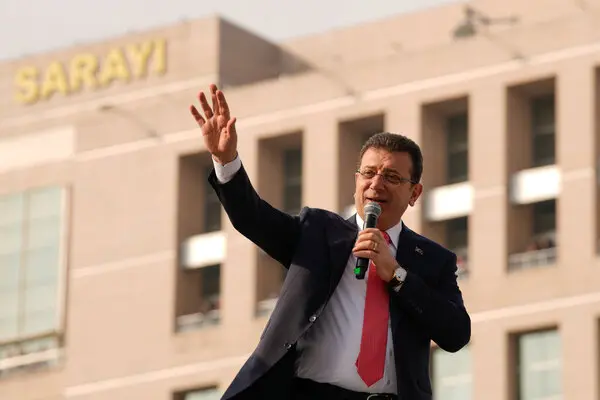 A man in a suit and tie waved while holding a microphone.