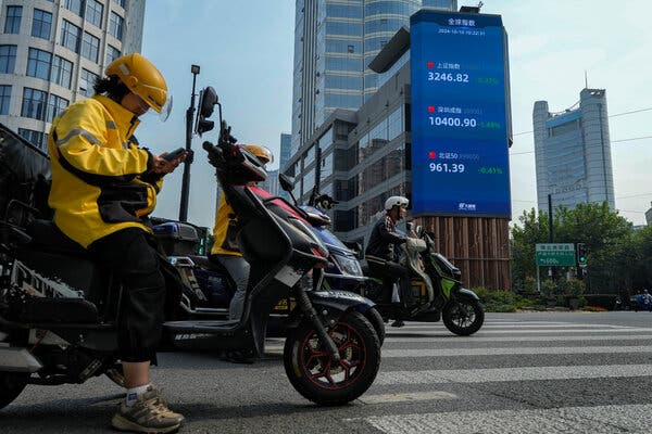 Several motor scooter riders, two wearing yellow safety helmets and one a white one, waiting at a zebra crossing for a traffic light to turn.