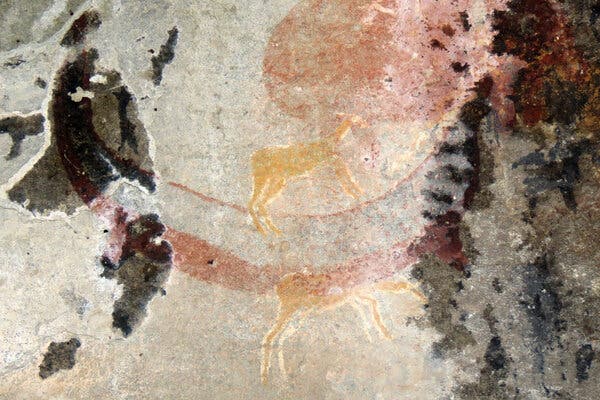 A few animals in faint yellow and red colors painted on a rock wall.