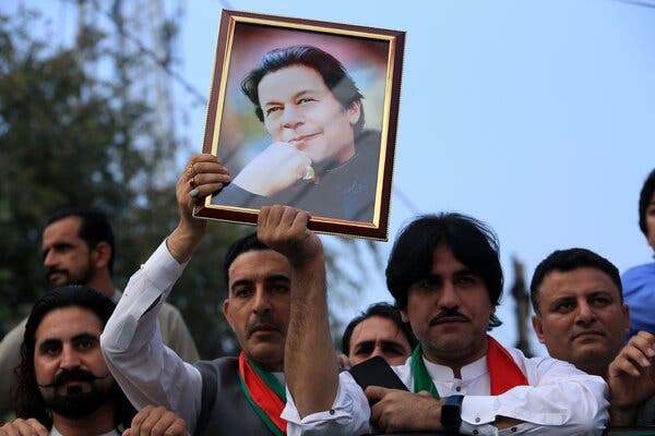 People stand outside in a rally. Two are holding up a portrait of Imran Khan.