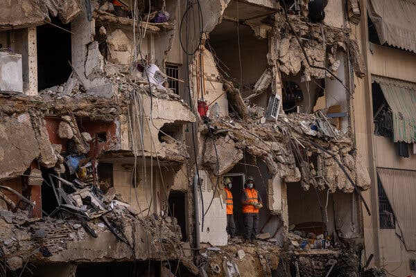 Two people in orange vests standing in a severely damaged building.