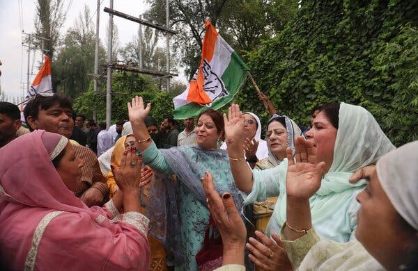 People clap and high-five in celebration outdoors. Many are wearing colorful saris. 