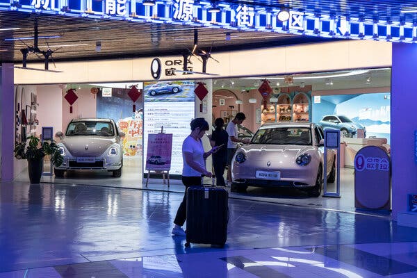 People walk inside a shopping center with cars on display. 